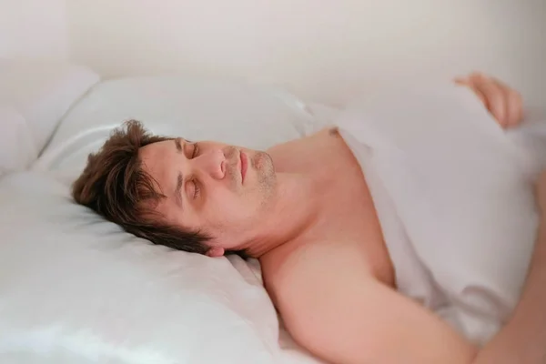 Ο άνθρωπος κοιμάται στο κρεβάτι μόνο κάτω από την κουβέρτα. Πλάγια όψη. — Φωτογραφία Αρχείου