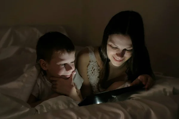 Мама и сын выбирают, что смотреть перед сном на планшете под одеялом . — стоковое фото