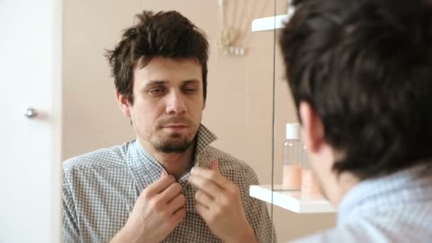 L'uomo stanco che si è appena svegliato guarda il suo riflesso nello specchio e vede il suo aspetto trasandato. Raddrizza la camicia e si strofina il viso con la mano . — Video Stock