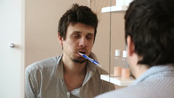 Замученный сонный человек просыпается только перед зеркалом с зубной щеткой во рту. . — стоковое видео