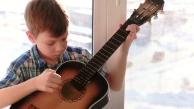 Bir enstrüman çalma. Çocuk pencere kenarında oturup gitar çalıyor.