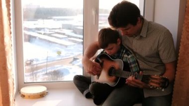 Bir enstrüman çalma. Baba oğlu kenarında oturup gitar çalmayı öğretir.