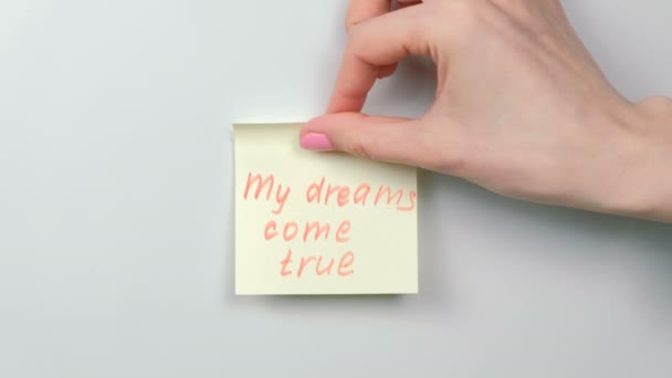 Closeup womans hands stick yellow sticker paper sheets with words my dreams come true. — Stock Video