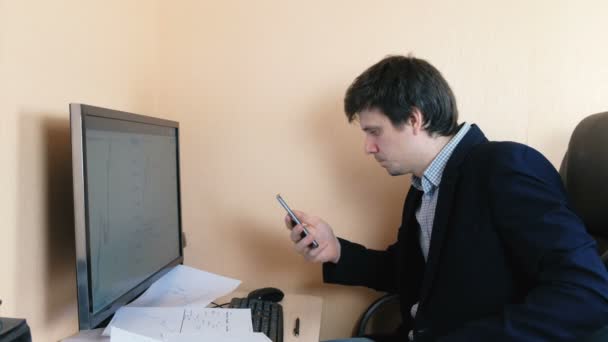 남자가는 컴퓨터에서 작업 하는 그의 휴대 전화 검색. — 비디오