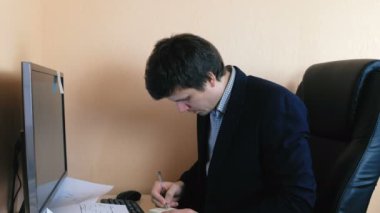 Bilgisayarda çalışan adam. Yazdığı bir şey etiket, kağıt ve ekranda sopa.