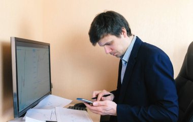 Bilgisayar ve cep telefonu bir deri sandalyede oturan genç adam çalışıyor