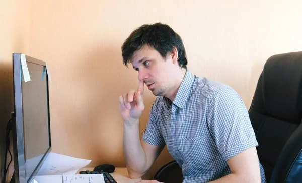 Young man picks his nose working at the computer.