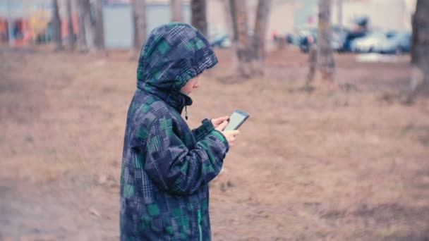 Αγόρι καλεί έναν αριθμό και να μιλάει σε ένα κινητό τηλέφωνο στο πάρκο. — Αρχείο Βίντεο