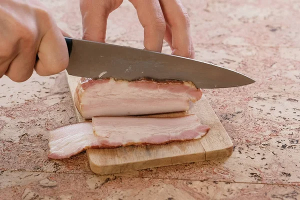 Человек режет свиную грудинку с беконом на ломтиках на деревянной доске. Рука крупного плана — стоковое фото