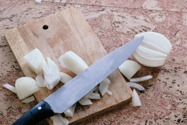 Knife and onion pieces on a wooden board