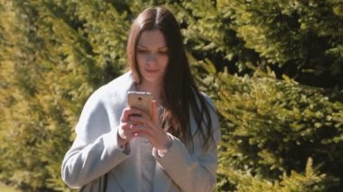 Güzel esmer telefonunu Park içinde bir ileti gönderme portresi. Yan görünüm.