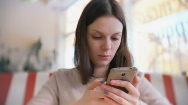 Junge schöne Frau brünett tippt und sendet Nachricht in ihr Handy im Café und wartet auf ihre Freunde. — Stockvideo