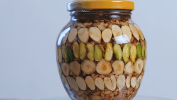 Rotating jar with nuts in honey. Close-up side view. — Stock Video