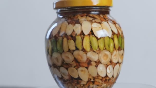 Rotating jar with nuts in honey. Close-up side view. — Stock Video