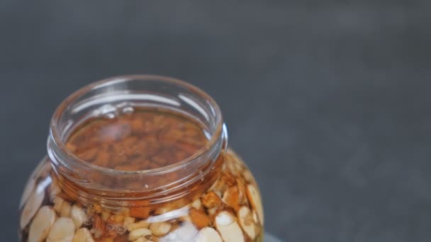 Rotating open jar with nuts in honey. Close-up top view. — Stock Video