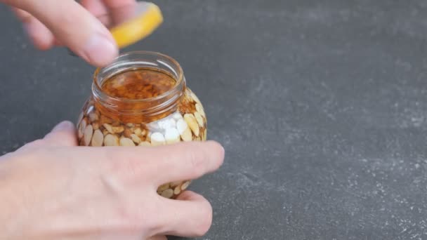 Man sluit het deksel van een pot van noten in de honing. Close-up van de handen. — Stockvideo