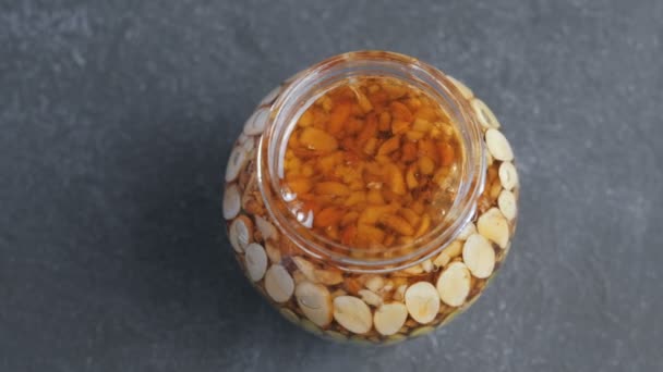 Open jar with nuts in honey on black table. Top view close-up. — Stock Video