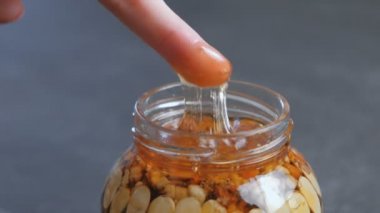 Kadın parmağını bal kavanozuna fındıklı dips. Yakın çekim el, parmak ve kavanoz siyah masada.