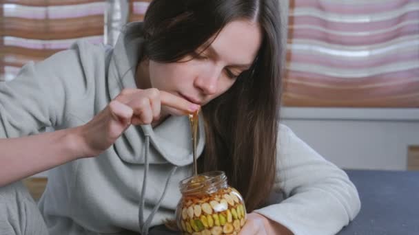 여자는 항아리에 견과류와 꿀에 그녀의 손가락을 담근 다. 손가락에서 먹는 꿀. — 비디오