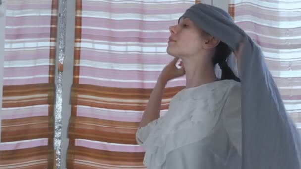 Mooie jongedame zet op grijs hoofddoek op haar hoofd staande voor de spiegel thuis. — Stockvideo