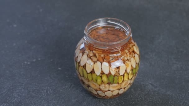 Open jar with nuts in honey on black table. — Stock Video