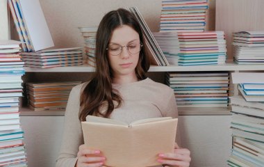 Bir kitap okuma gözlüklü genç esmer kadın. Kitaplar arasında oturan