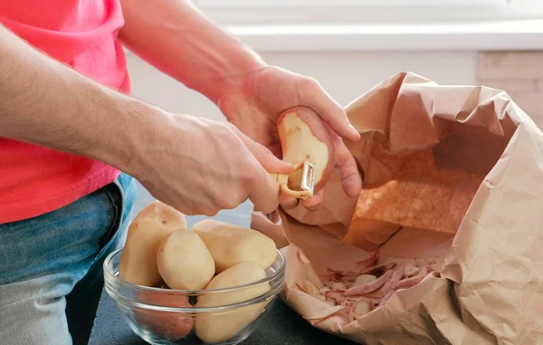 Ман чистит картошку руками. Бумажный пакет с очисткой картошки. Картошка в миске — стоковое фото