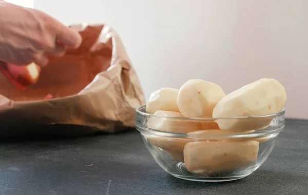 Tangan Mans mengupas kentang. Kantong kertas dengan membersihkan kentang. Kentang dalam mangkuk. Tampilan atas . — Stok Foto