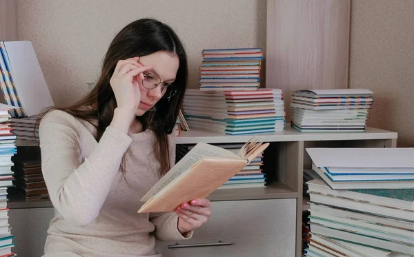 stock image Young brunette woman wearing glasses read book sitting on the floor among the books.