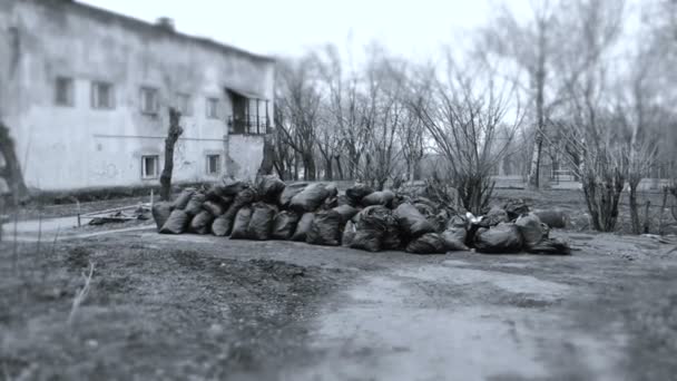 Black trash bags piled up In the city against house. Black and white. — Stock Video