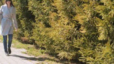 Genç esmer kadın güneş gözlüğü ve ceket Şehir Parkı içinde yürür. Bahar.