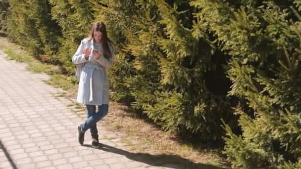 Jonge brunette vrouw in vacht ziet er op de navigatiekaart in je telefoon te vinden van het pad in de stad. — Stockvideo