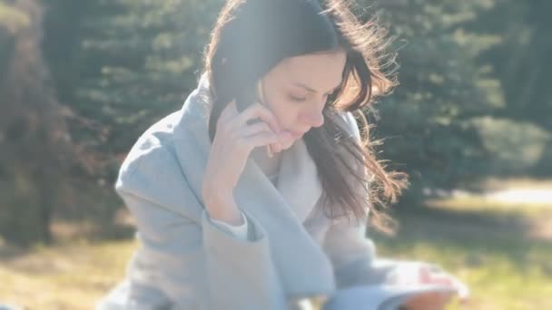 Portrait de femme animée assise dans le parc du printemps sur l'herbe et parlant sur un téléphone portable . — Video