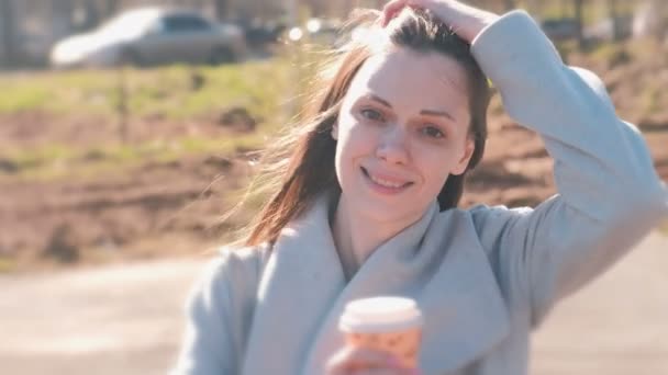 Portrait de jolie jeune femme brune souriante dans le parc de la ville avec du café . — Video