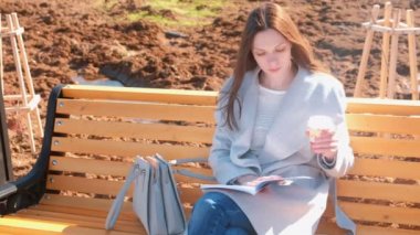 Genç güzel esmer kadın öğrenci bahar parkta bankta oturur kitap ve içecekler kahve okur.