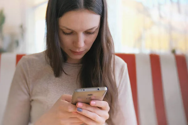 Junge schöne Frau brünett tippt und sendet Nachricht in ihr Handy im Café und wartet auf ihre Freunde. — Stockfoto