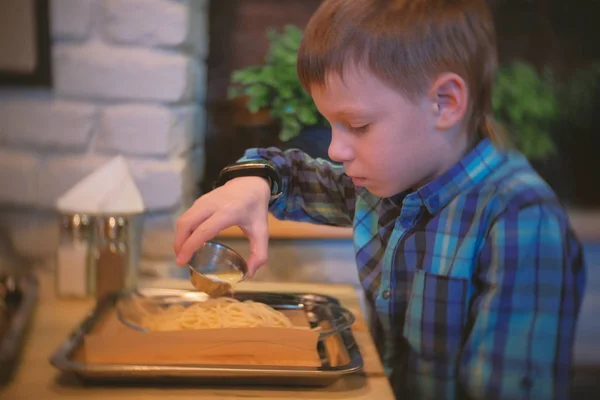 Chłopiec rozlewa masła do spaghetti. Widok z boku. — Zdjęcie stockowe