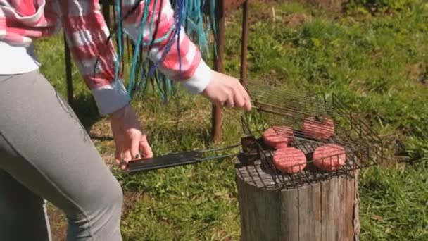 Felismerhetetlen fiatal nő bezárja a grill, és a hússzeleteket. Közeli kezek. Ő van kockás rózsaszín inget és kék zsinór szőrszálak. — Stock videók