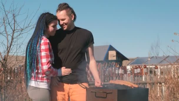 Man en een vrouw cook hamburgers op de grill samen, knuffel en kus. — Stockvideo