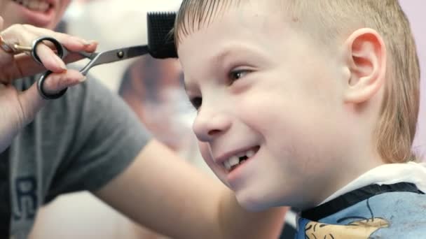 Closeup barbers hands combs and cut bangs on blond short boys hair with scissors. — Stock Video