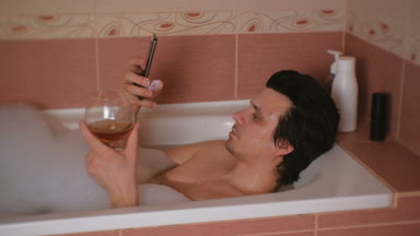 Genç adam bir banyo köpüğü, türleri haber üstünde hareket eden telefon ve içki viski ve gülümsüyor ile alır.