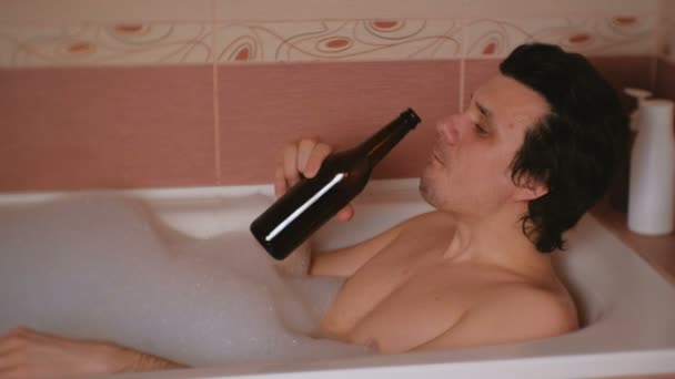 Genç adam bir banyo köpüğü ile alır ve bira içiyor. Gülümseyen ve kameraya bakıyor. — Stok video