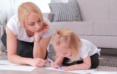 Küçük sevimli sarışın kız kanepede oturan annesi ile mor keçe-kalem boyama.