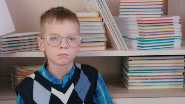 Unavený sedm rok starý chlapec s brýlemi, sedí na podlaze mezi knihami. — Stock video