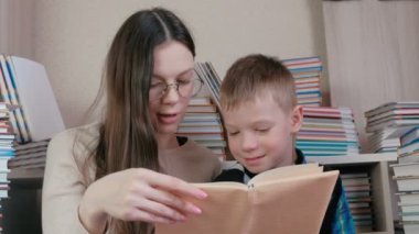 Anne, kitaplar arasında oturan oğlu için bir kitap okuyun. Anne gözlük.