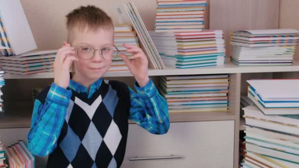 Lächelnder siebenjähriger Junge mit Brille auf dem Boden zwischen den Büchern. — Stockvideo