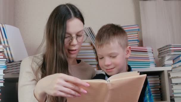Mom は、本の中で座っている彼女の息子のための本を読みます。メガネでママは. — ストック動画