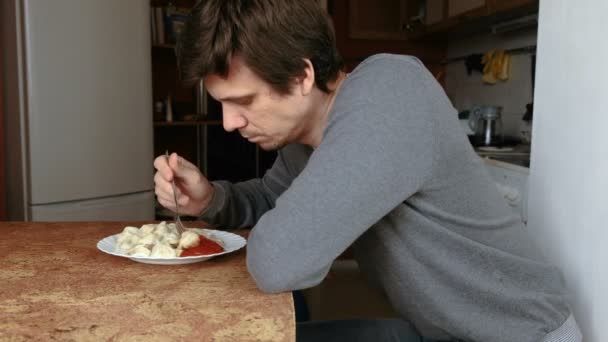 L'uomo mangia gnocchi con una forchetta, mettendoli in salsa di pomodoro in cucina. . — Video Stock