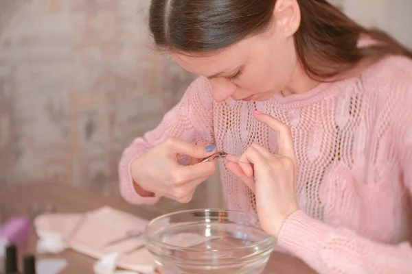 La mujer corta la cutícula con una pinza. Hace la manicura ella misma. Herramientas de manicura sobre la mesa . —  Fotos de Stock