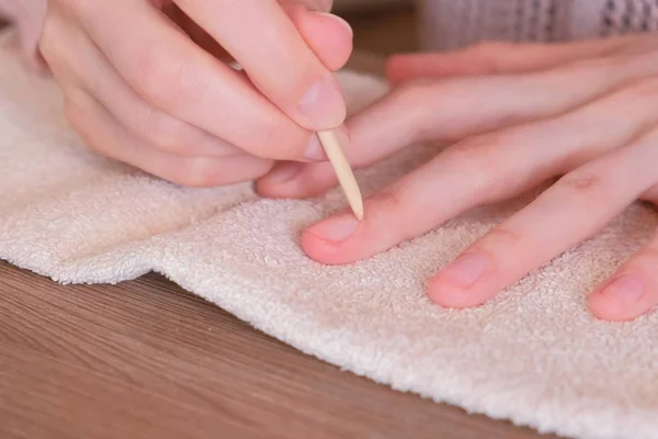 Mulher limpa o excesso de unhas polonês usando pau de madeira laranja para manicure . — Fotografia de Stock